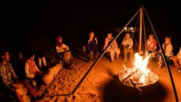 A group of people gathered around a campfire on a sandy beach at night.