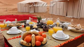 Mesa al aire libre con temática desértica, ofreciendo diversos alimentos para el desayuno, como frutas, pan y bebidas.