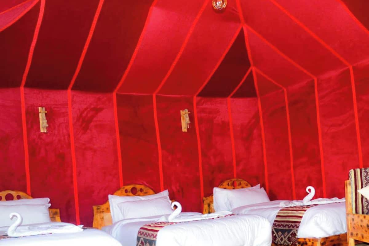 A tent-style room with three beds, each with a wooden headboard and white bedding.
