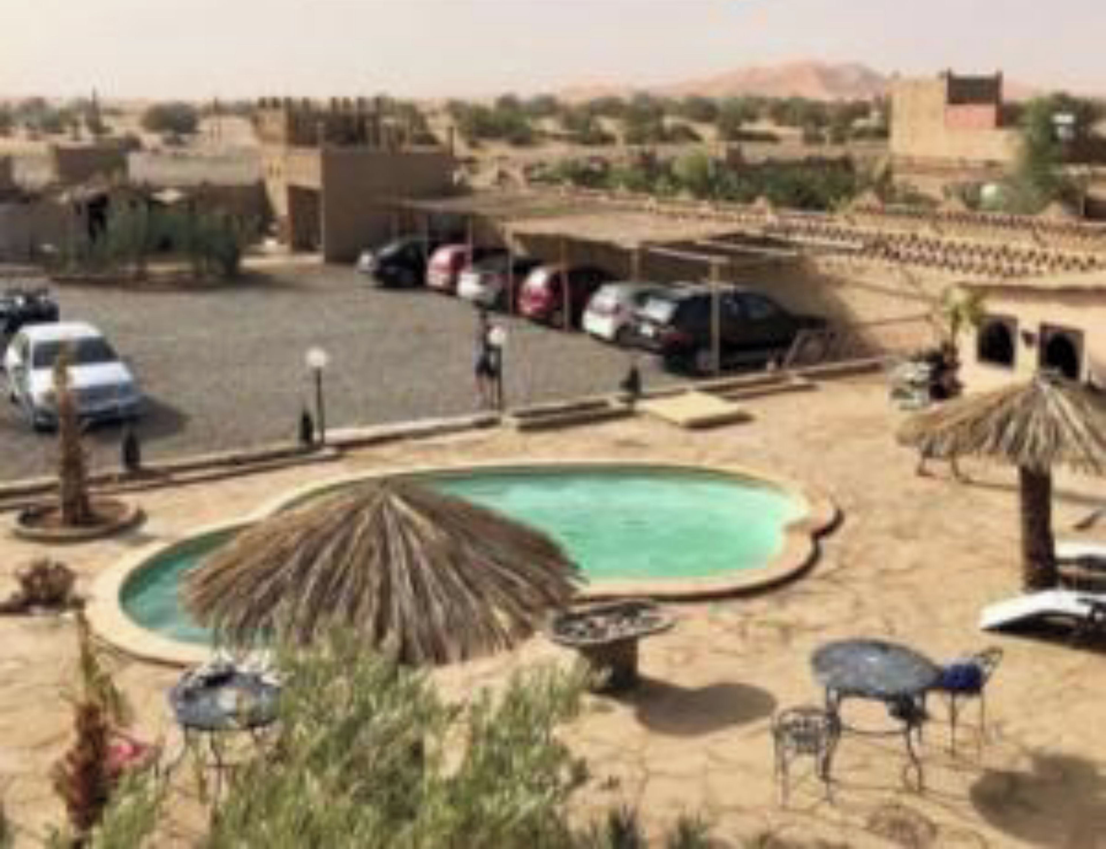Un espace de stationnement avec plusieurs voitures, une piscine et, au loin, un paysage désertique.