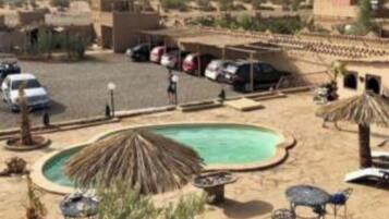 Un espace de stationnement avec plusieurs voitures, une piscine et, au loin, un paysage désertique.