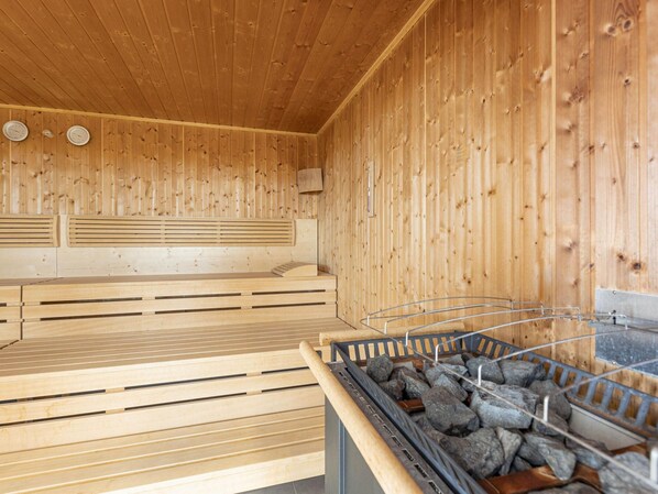 A sauna room with wooden walls and benches, a heater, and a stone basin.