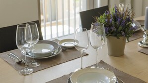 Een eettafel gedekt met borden, glazen en bestek, met een potplant en kaarsen op tafel.