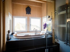A modern bathroom with a freestanding bathtub, two windows, a Buddha statue, and a glass shower enclosure. - Quiet Chalet in Turracherhöhe with Sauna & Indoor Hot Tub (Stadl-Predlitz)