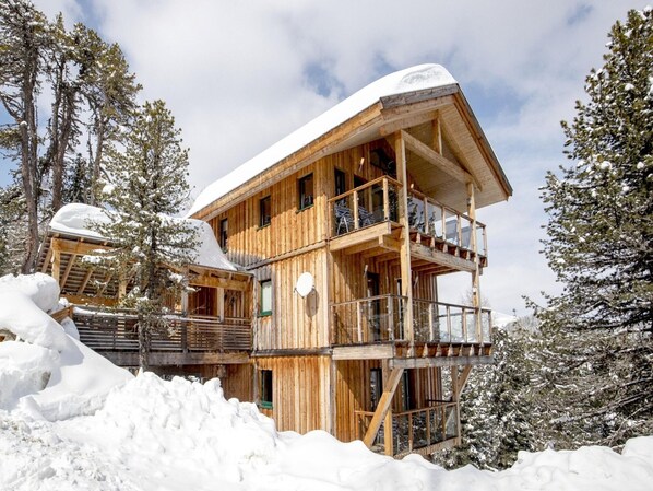 A wooden chalet with a balcony and a snow-covered roof, surrounded by trees. - Quiet Chalet in Turracherhöhe with Sauna & Indoor Hot Tub (Stadl-Predlitz)