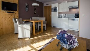 A compact living space with a dining area, kitchenette, and a flat-screen TV mounted on a wooden wall. - Cozy Apartment near Ski Area in Turracherhohe (Stadl-Predlitz)