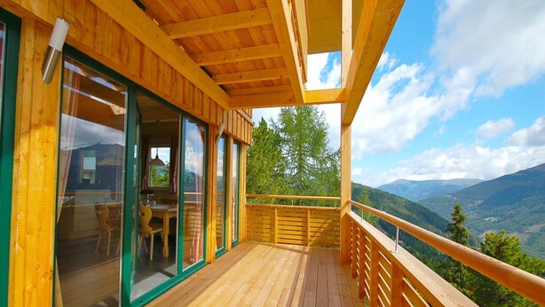 A wooden deck with a glass door leading to an interior space, a wooden railing, and a view of a mountainous landscape.
