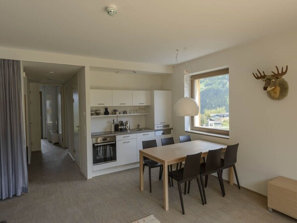 A modern kitchen with white cabinets, a dining area with a wooden table and chairs, and a window with a view of a forest. - Beautiful Apartment With Private Sauna (Schladming)