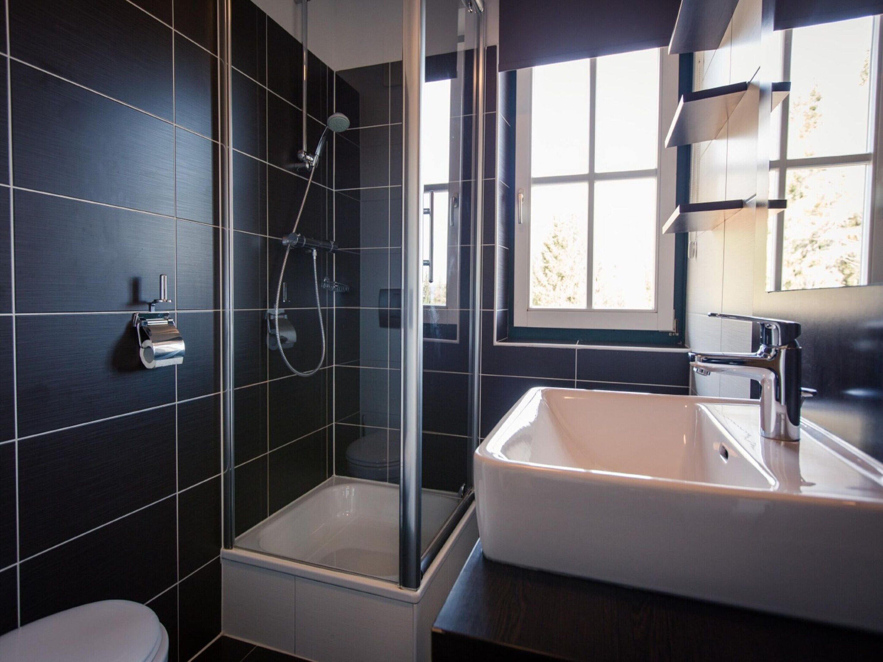 A modern bathroom with a glass-enclosed shower, a white sink, and a toilet.