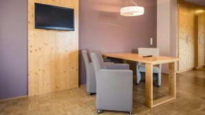 A modern room with a wooden wall panel, a flat-screen TV mounted above a wooden table, and a ceiling fan. - Studio Apartment on Turracherhohe Near Lake (Stadl-Predlitz)