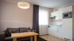 A modern living room with a sofa, a wooden table, and a kitchen area with white cabinets and a microwave. - Studio Apartment on Turracherhohe Near Lake (Stadl-Predlitz)