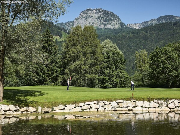 A golf course with a pond and stone wall, surrounded by trees and mountains. - Welcoming Apartment Near ski Slopes (Schladming)