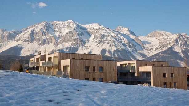Un edificio moderno con diversi piani e balconi, sullo sfondo di montagne innevate.