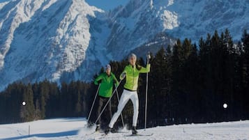 Zwei Personen rodeln einen schneebedeckten Hang hinunter, im Hintergrund erstreckt sich ein Gebirgszug.