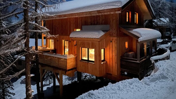Eine Holzhütte mit Balkon, mehreren Fenstern und einem mit Schnee bedeckten Dach.