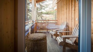 Eine Holzterrasse mit Außenmöbeln, darunter Stühle und Tische, sowie ein Korbwägelchen.