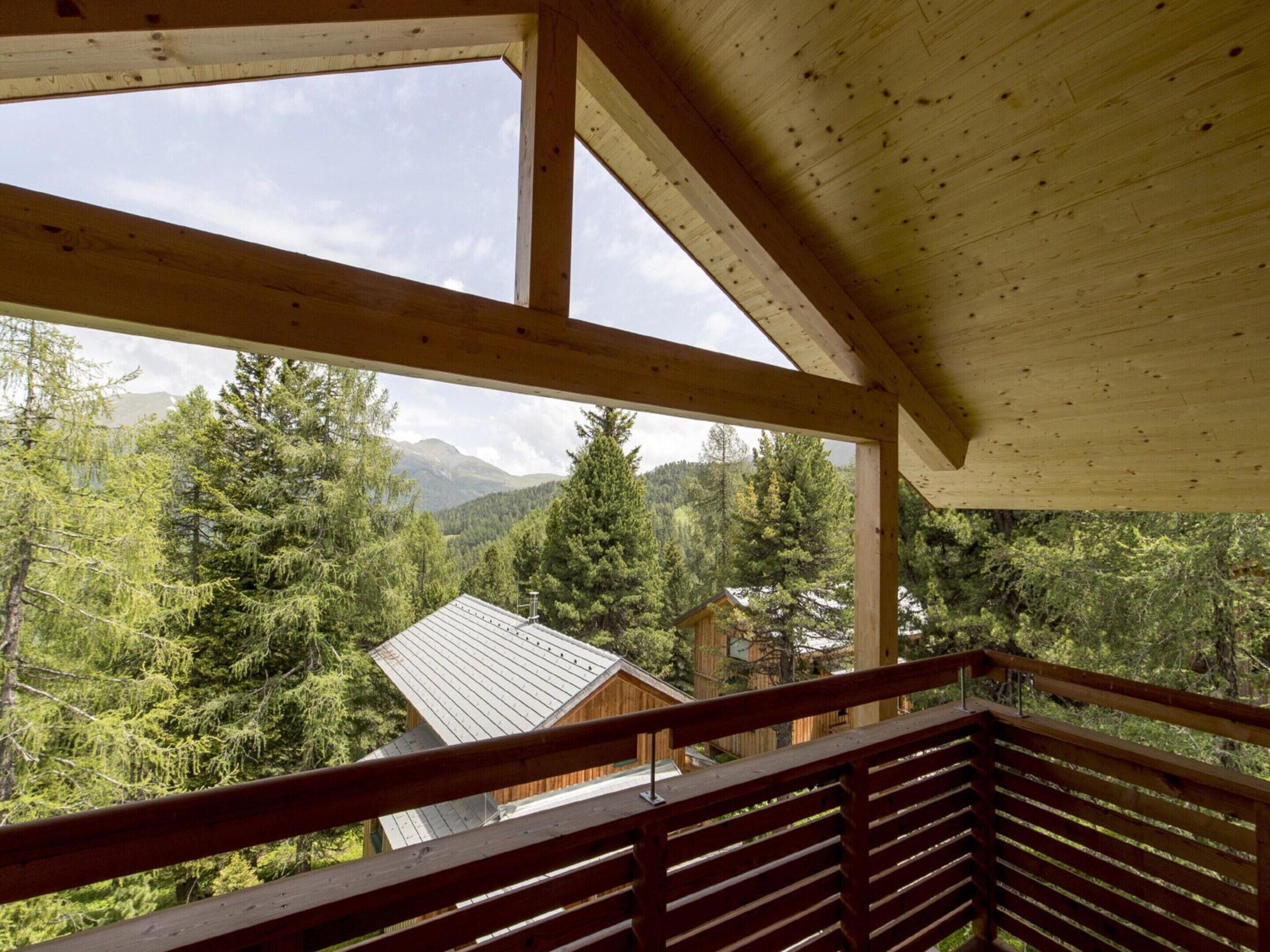 A wooden cabin with a balcony overlooking a forested mountain area.