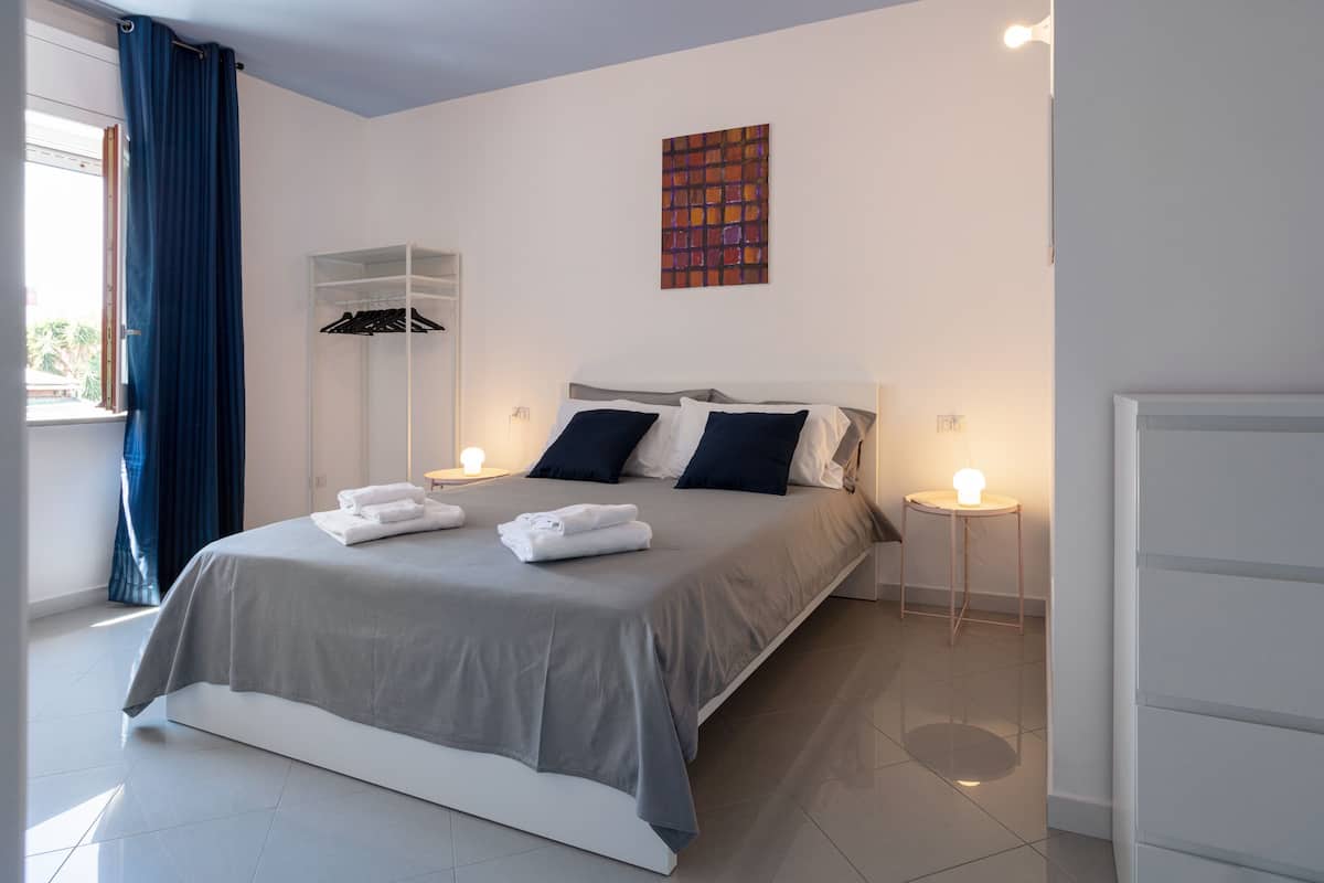A modern bedroom with a large bed, bedside tables, a wardrobe, and a window with curtains.
