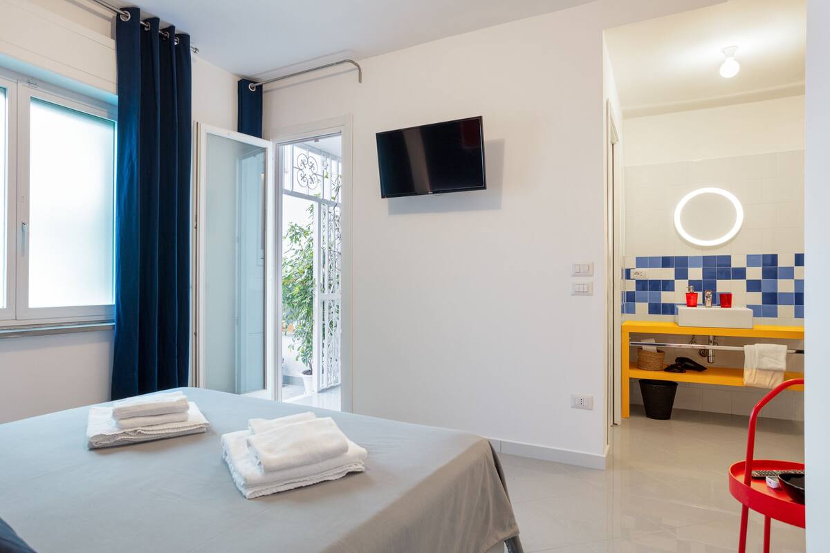 A hotel room with a bed, a TV mounted on the wall, a bathroom with a sink and mirror, and a view of the outdoors.