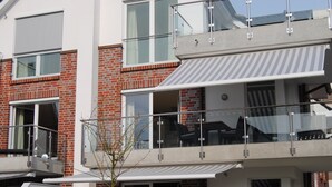 Um edifício residencial de vários andares com fachada de tijolos, grandes janelas e uma varanda com guarda-corpo de vidro.