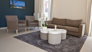 Uma sala de estar moderna com um sofá marrom, duas poltronas e uma mesa de centro com um vaso de flores brancas.