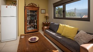Una sala de estar con un sofá, una mesa de centro de madera, un mueble con puertas de vidrio, un refrigerador blanco y una ventana con vistas al exterior.