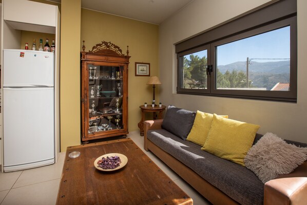 A living room with a sofa, a wooden coffee table, a cabinet with glass doors, a white refrigerator, and a window with a view of the outdoors.