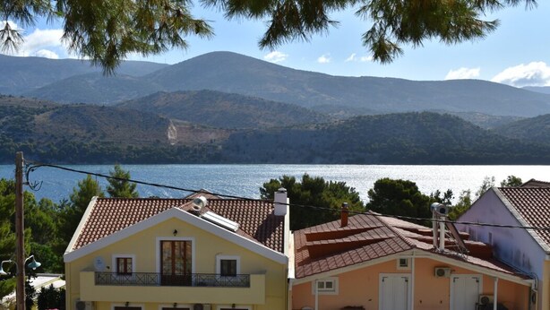 Un edificio costero con balcón, techo de tejas y vistas al mar y a las montañas.