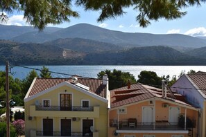 A coastal building with a balcony, a tiled roof, and a view of the sea and mountains.