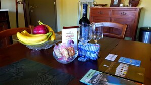 Una mesa de comedor con un bol de fruta, una botella de vino, copas y un menú.