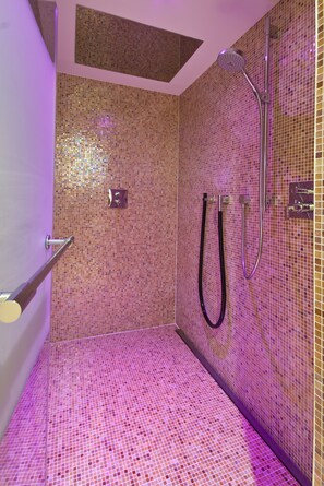 Una ducha con paredes de mosaicos y cabezal de ducha manual.