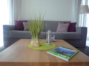 Un salon avec un canapé gris, une table basse, un livre et un vase contenant des plantes vertes.