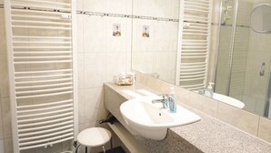 Un baño con lavamanos blanco, un espejo y cabina de ducha.