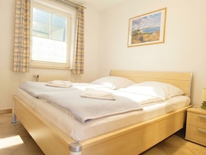 A bedroom with a bed, a window with curtains, a bedside table, and a wall-mounted picture. - WM110 House with Ocean View - WM110 (Kühlungsborn)