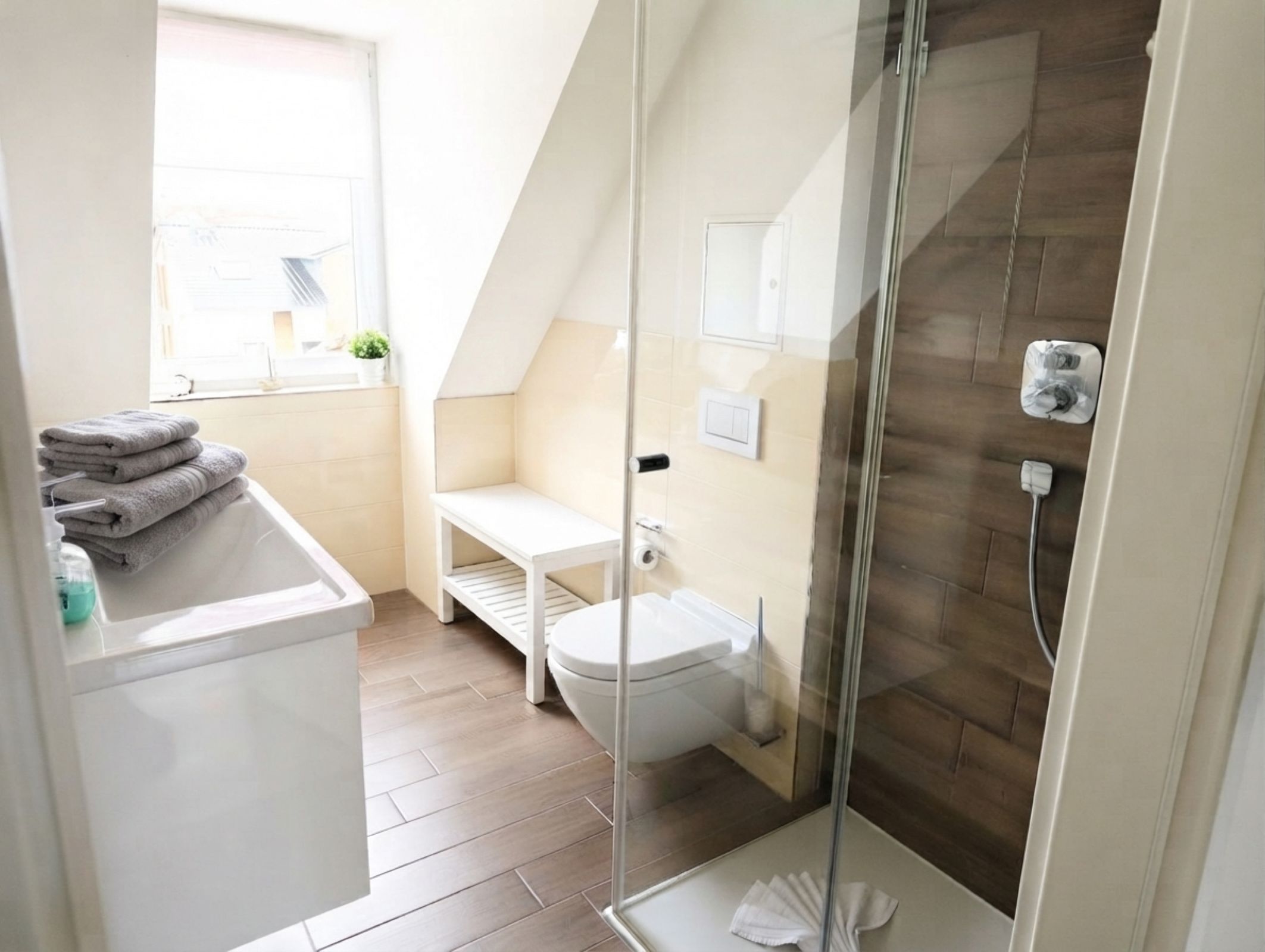 A modern bathroom with a glass shower enclosure, a toilet, and a sink area with towels.