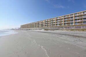 A beachfront hotel with multiple balconies, a sandy beach, and a clear sky. - Stay @ A View to Remember on Folly Beach (Folly Beach)
