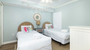 A bedroom with two beds, a ceiling fan, a nightstand, a lamp, and a wall decoration. - Stay @ A View to Remember on Folly Beach (Folly Beach)
