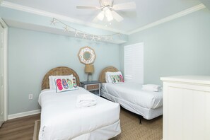 A bedroom with two beds, a ceiling fan, a nightstand, a lamp, and a wall decoration. - Stay @ A View to Remember on Folly Beach (Folly Beach)