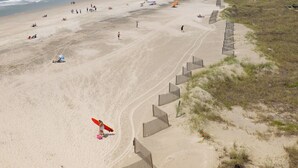 A beach with a sandy shore, a wooden fence, and a person with a red surfboard. - Stay @ A View to Remember on Folly Beach (Folly Beach)