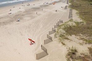 A beach with a sandy shore, a wooden fence, and a person with a red surfboard. - Stay @ A View to Remember on Folly Beach (Folly Beach)