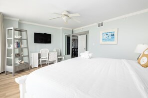 A hotel room with a large bed, a ceiling fan, a television, a bookshelf, a desk, and a chair.