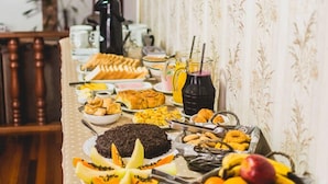 A buffet table with various food items and drinks, set against a patterned wallpaper background. - Sonho Da Serra Pousada (Bento Gonçalves)