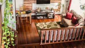 A living room with a wooden floor, a sofa with red cushions, a coffee table with decorative items, a TV mounted on the wall, and a staircase with wooden railings. - Sonho Da Serra Pousada (Bento Gonçalves)