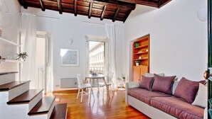 Een moderne woonkamer met een houten trap, een bank, een eettafel met stoelen en een boekenkast.