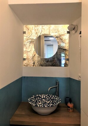 A bathroom with a round mirror, a vessel sink, and a stone wall backdrop. - Ca' del Monica Guesthouse (Riomaggiore)