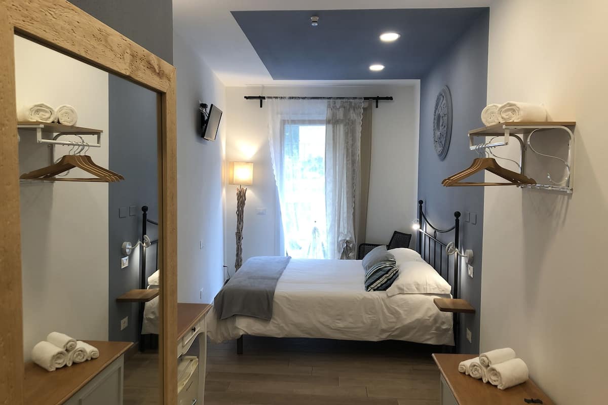 A bedroom with a bed, bedside tables, a mirror, a lamp, and a window with curtains.