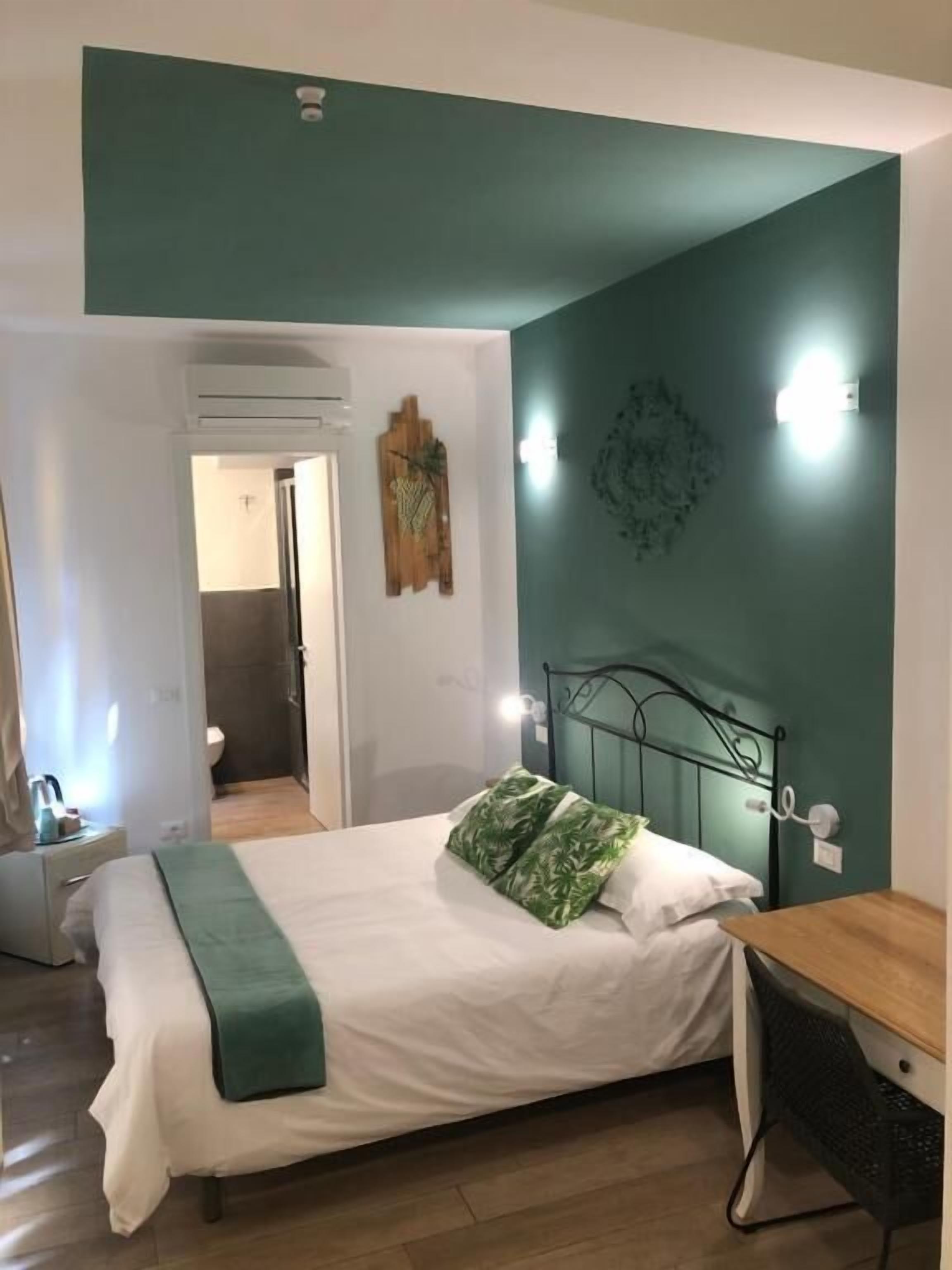 Ein Schlafzimmer mit Bett, Nachttisch, Schreibtisch und Stuhl. Eine Tür führt ins Bad.