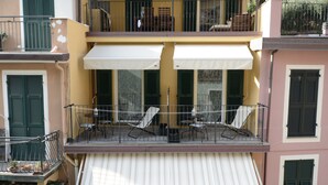 A multi-story building with a balcony featuring outdoor seating and a white awning.