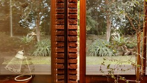 A window with a brick pattern, a hanging light fixture, and a view of a garden with trees and plants. - Pensão Favorita (Porto)