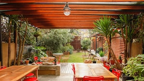 An outdoor patio with wooden tables and red chairs, surrounded by potted plants and a brick wall. - Pensão Favorita (Porto)